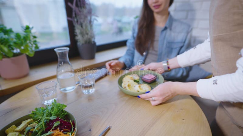 Il cameriere in un caffè accogliente ha portato un piatto vegetariano per un paio di visitatori. lo staff serve un uomo e una donn archivi video