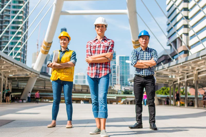 Il casco di sicurezza di usura dell'ingegnere industriale tre che costruisce la condizione con le armi ha attraversato la tenuta fotografia stock Il casco di sicurezza di usura dell'ingegnere industriale tre che costruisce la condizione con le armi ha attraversato la tenuta fotografia stock