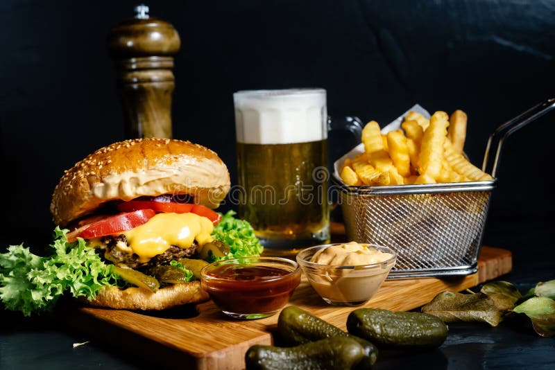 Il cheeseburger succoso con l'insalata delle fritture, dei sottaceti, della birra e dell'insalata di cavoli è servito dai bistrot fotografie stock libere da diritti