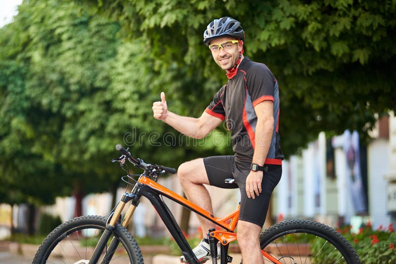 Il ciclista felice che mostra i pollici aumenta la bici di guida
