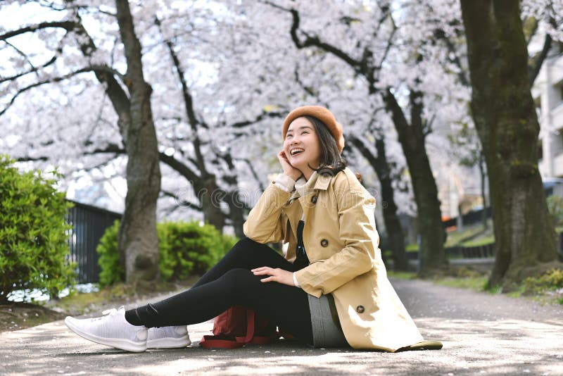 Il ciliegio Sakura fiorisce di fiori e una donna asiatica sorridente seduta sotto l'albero di fiori rosa immagine stock libera da diritti
