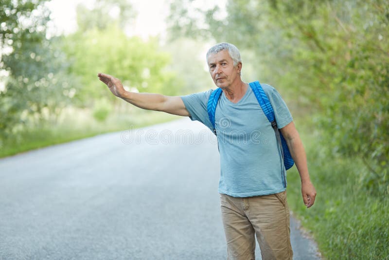 Il colpo all'aperto dell'uomo senior dai capelli grigio in maglietta casuale, ha viaggio di vacanza, fa auto-stop sulla strada in immagini stock Il colpo all'aperto dell'uomo senior dai capelli grigio in maglietta casuale, ha viaggio di vacanza, fa auto-stop sulla strada in immagini stock
