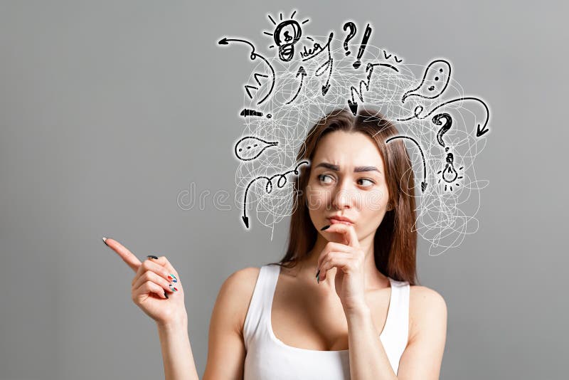 The concept of searching for ideas and information. Portrait of a pensive young Caucasian woman looking sideways, pointing her finger to the side, with painted icons and doodles above her head. Gray background. Copy space. The concept of searching for ideas and information. Portrait of a pensive young Caucasian woman looking sideways, pointing her finger to the side, with painted icons and doodles above her head. Gray background. Copy space.