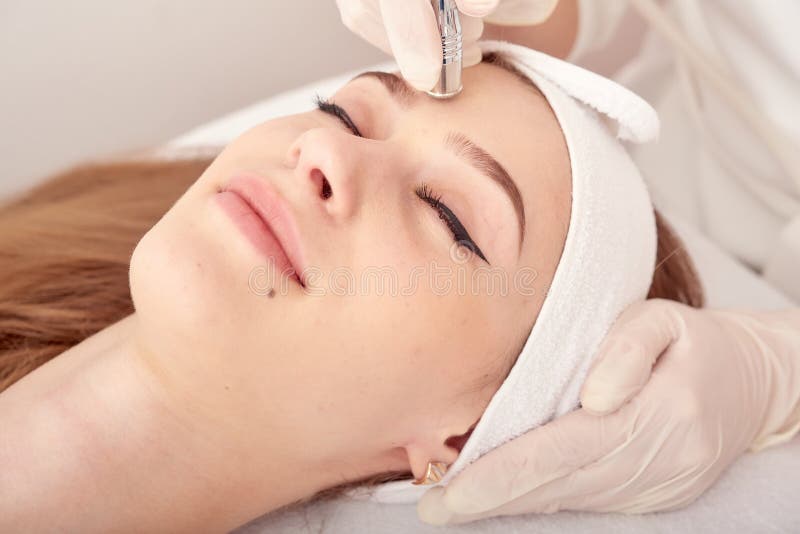 Il cosmetologo fa la procedura Microdermabrasion della pelle facciale di un bello, giovane donna in un salone di bellezza immagini stock libere da diritti Il cosmetologo fa la procedura Microdermabrasion della pelle facciale di un bello, giovane donna in un salone di bellezza immagini stock libere da diritti