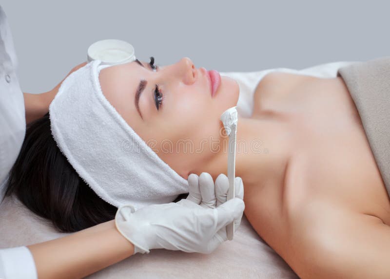 Il cosmetologo per la procedura di pulizia e di idratazione della pelle, applicante una maschera con il bastone al fronte di giov fotografia stock Il cosmetologo per la procedura di pulizia e di idratazione della pelle, applicante una maschera con il bastone al fronte di giov fotografia stock