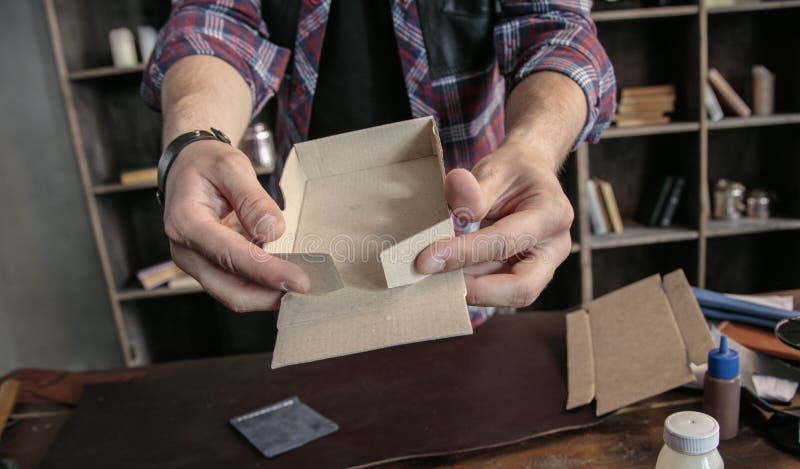 Il creatore del cuoio del giovane monta manualmente il contenitore d'imballaggio di cartone per i prodotti