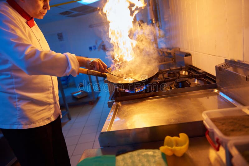 Il cuoco unico nella cucina dell'hotel prepara l'alimento con fuoco fotografia stock Il cuoco unico nella cucina dell'hotel prepara l'alimento con fuoco fotografia stock