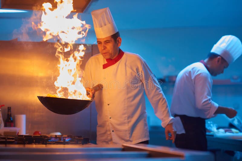 Il cuoco unico nella cucina dell'hotel prepara l'alimento con fuoco fotografia stock libera da diritti Il cuoco unico nella cucina dell'hotel prepara l'alimento con fuoco fotografia stock libera da diritti
