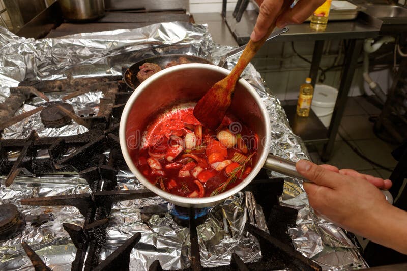 Il cuoco unico sta cucinando le verdure con il succo della barbabietola, producente la salsa per carne fotografia stock Il cuoco unico sta cucinando le verdure con il succo della barbabietola, producente la salsa per carne fotografia stock