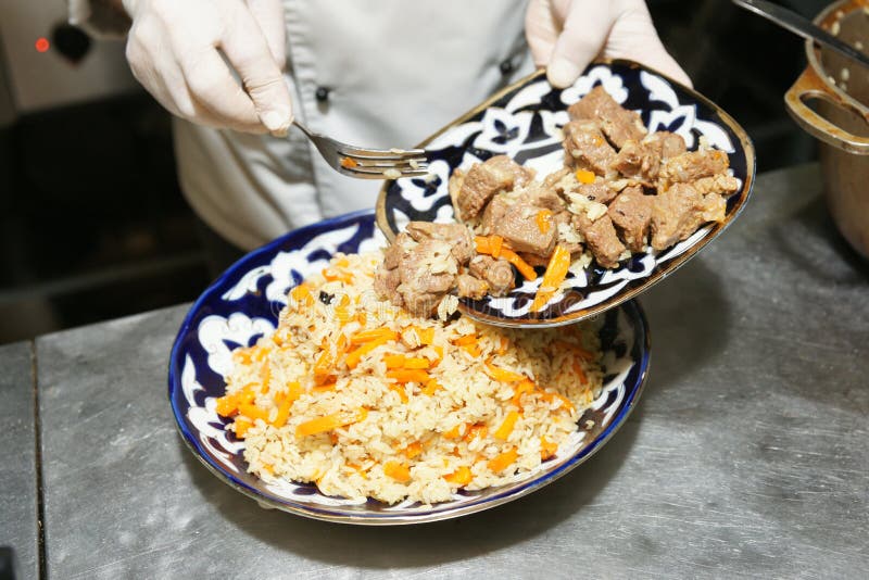 Il cuoco unico sta servendo il pilaf nella cucina del ristorante immagine stock Il cuoco unico sta servendo il pilaf nella cucina del ristorante immagine stock