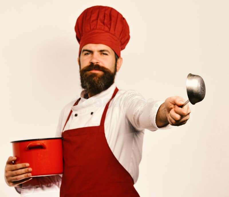 Chef holds soup or compote. Restaurant cuisine concept. Man with beard holds red pot on white background. Cook with happy face in burgundy uniform has casserole with ladle. Chef holds soup or compote. Restaurant cuisine concept. Man with beard holds red pot on white background. Cook with happy face in burgundy uniform has casserole with ladle.