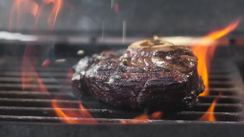 Il cuoco versa il pepe sulla carne sulla griglia Lotti di fuoco Movimento lento, primo piano