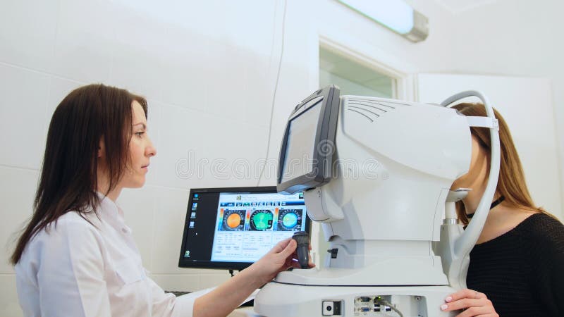 Il ` d'esame s della donna dell'oftalmologo osserva con l'attrezzatura di ciao-tecnologia nel centro medico immagine stock Il ` d'esame s della donna dell'oftalmologo osserva con l'attrezzatura di ciao-tecnologia nel centro medico immagine stock