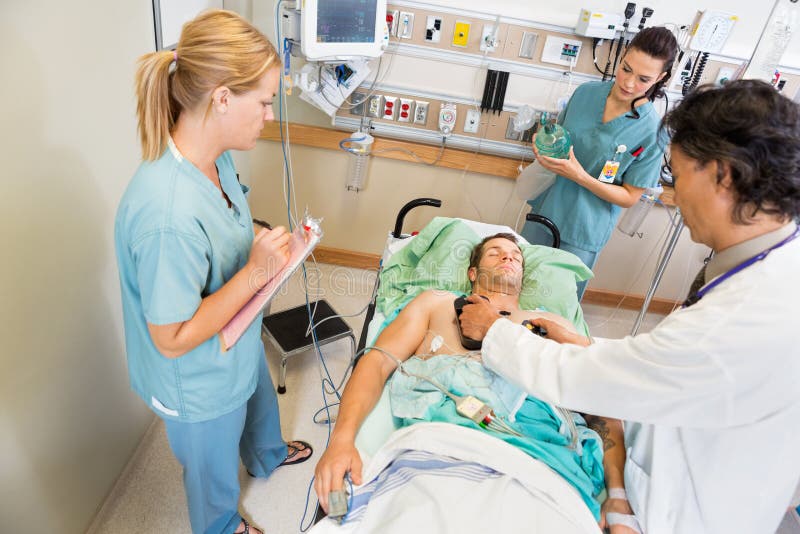 High angle view of doctor defibrillating critical patient while nurses standing by in hospital. High angle view of doctor defibrillating critical patient while nurses standing by in hospital