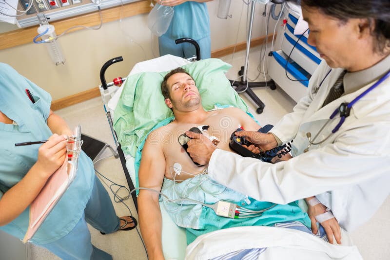 High angle view of doctor defibrillating male patient while nurses standing by in hospital. High angle view of doctor defibrillating male patient while nurses standing by in hospital