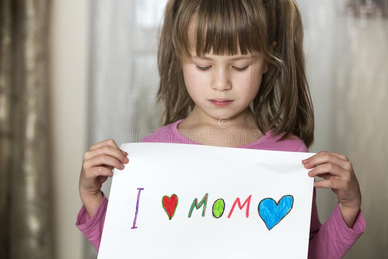Il foglio di carta di spirito della ragazza del bambino sveglio con i pastelli variopinti ha dipinto le parole che amo la mamma E immagini stock Il foglio di carta di spirito della ragazza del bambino sveglio con i pastelli variopinti ha dipinto le parole che amo la mamma E immagini stock