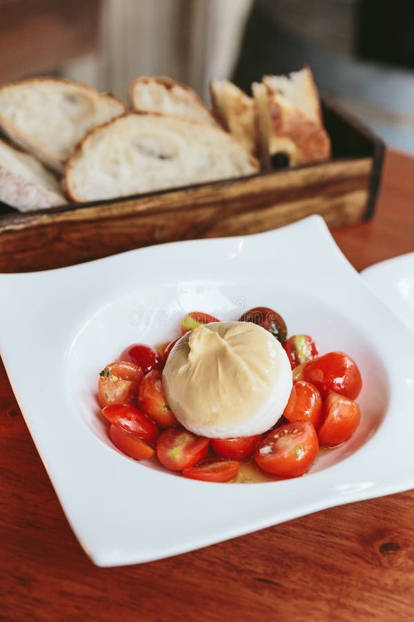 Il formaggio di Burrata con l'insalata del confit del pomodoro ciliegia è servito in piatto bianco sulla tavola di legno immagine stock Il formaggio di Burrata con l'insalata del confit del pomodoro ciliegia è servito in piatto bianco sulla tavola di legno immagine stock