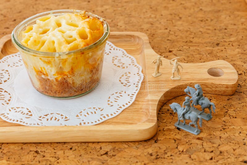 Il formaggio ha cotto Penne in ciotola di vetro sul piatto di legno con i soldati ed i cavalli da equitazione miniatura dei cowbo immagini stock Il formaggio ha cotto Penne in ciotola di vetro sul piatto di legno con i soldati ed i cavalli da equitazione miniatura dei cowbo immagini stock