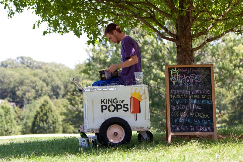 Atlanta, GA, USA - July 28, 2012: An unidentified ice cream vendor reads a book to pass the time as he waits for customers in an Atlanta public park. The vendor was waiting for an organized water gun fight to start. Atlanta, GA, USA - July 28, 2012: An unidentified ice cream vendor reads a book to pass the time as he waits for customers in an Atlanta public park. The vendor was waiting for an organized water gun fight to start.