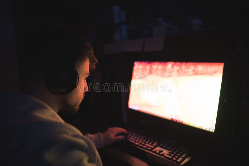 Il Gamer gioca i giochi di computer in una stanza scura l'uomo nelle cuffie gioca i giochi di computer alla notte Concetto del Ga fotografia stock Il Gamer gioca i giochi di computer in una stanza scura l'uomo nelle cuffie gioca i giochi di computer alla notte Concetto del Ga fotografia stock
