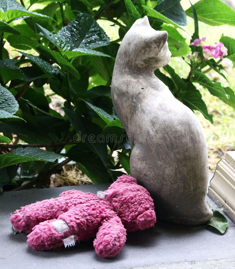 Il gatto di pietra con l'orsacchiotto rosa inzuppato riguarda il portico fotografia stock Il gatto di pietra con l'orsacchiotto rosa inzuppato riguarda il portico fotografia stock