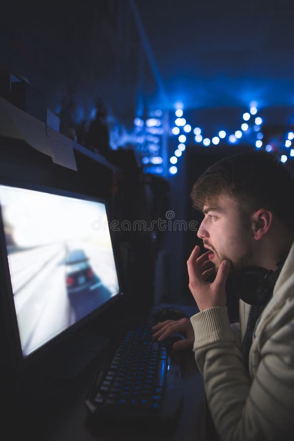 Il giovane con una barba gioca i giochi di computer a casa alla notte Il Gamer gioca su un computer in una stanza accogliente fotografie stock Il giovane con una barba gioca i giochi di computer a casa alla notte Il Gamer gioca su un computer in una stanza accogliente fotografie stock