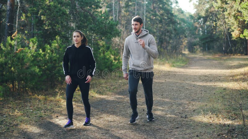 Il giovane delle coppie sveglie e sua l'amica stanno facendo gli sport in parco che fa insieme gli esercizi che godono simultanea