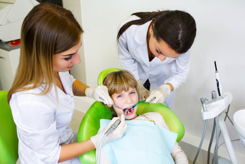 Il giovane dentista bello cura il bambino del dente, un dentista della donna immagini stock libere da diritti Il giovane dentista bello cura il bambino del dente, un dentista della donna immagini stock libere da diritti