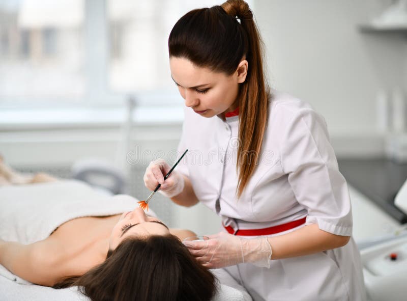 Il giovane estetista molto è messo a fuoco durante preparare il paziente per una procedura cosmetica Applica delicatamente una co fotografie stock Il giovane estetista molto è messo a fuoco durante preparare il paziente per una procedura cosmetica Applica delicatamente una co fotografie stock