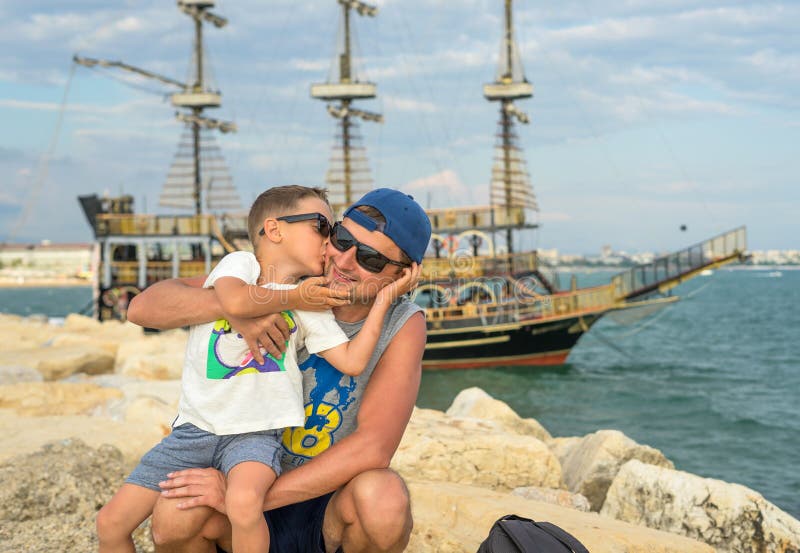 Il giovane padre sorridente bacia il figlio vicino al mare sul tramonto Giorni di estate felici Concetto della famiglia amichevol fotografie stock libere da diritti Il giovane padre sorridente bacia il figlio vicino al mare sul tramonto Giorni di estate felici Concetto della famiglia amichevol fotografie stock libere da diritti