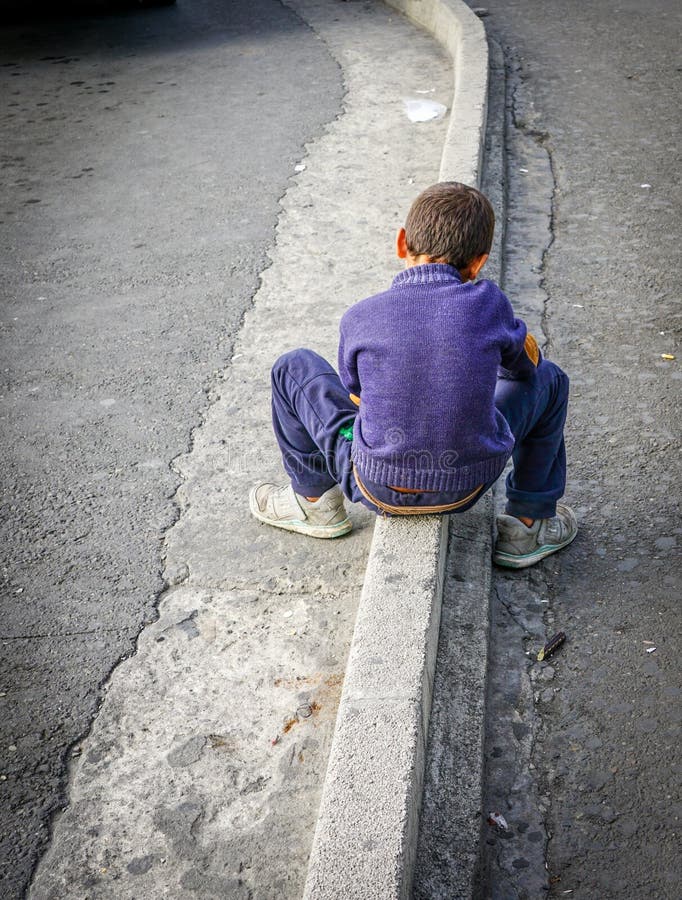 Il giovane ragazzo in maglione porpora e blue jeans si siede sul confine della via fotografie stock libere da diritti Il giovane ragazzo in maglione porpora e blue jeans si siede sul confine della via fotografie stock libere da diritti