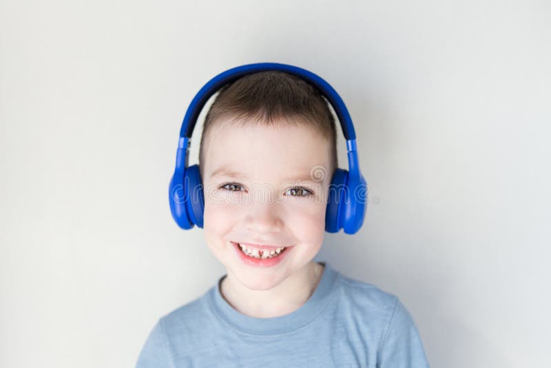 Il giovane ragazzo ? sorridente ed ascoltante la musica in cuffie blu, stanti davanti alla parete bianca Copi lo spazio fotografie stock Il giovane ragazzo ? sorridente ed ascoltante la musica in cuffie blu, stanti davanti alla parete bianca Copi lo spazio fotografie stock