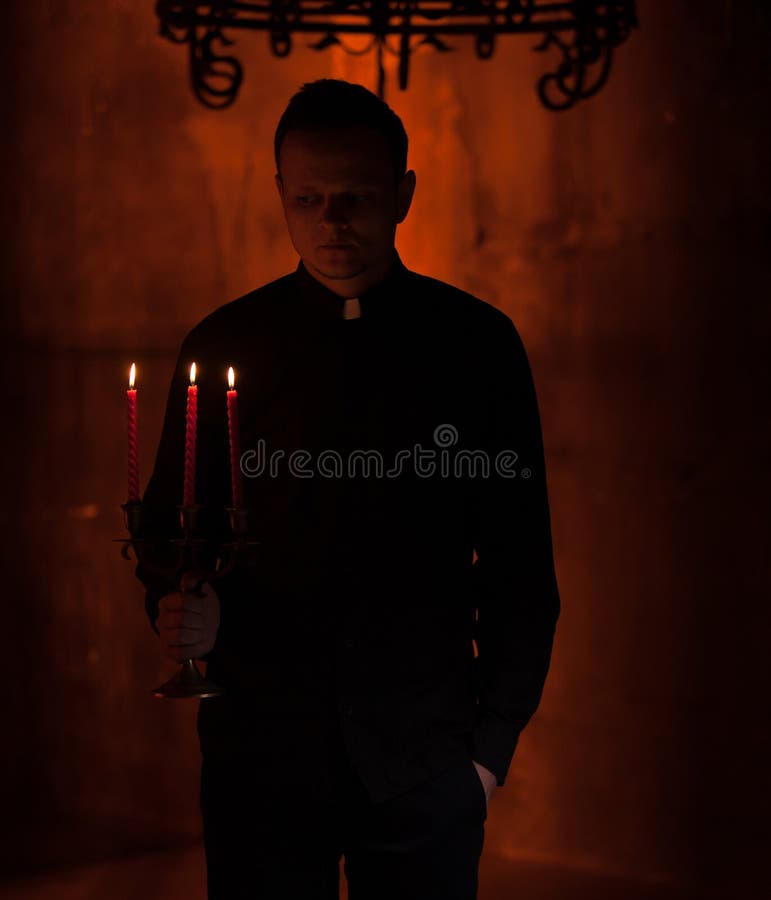 Il giovane sacerdote pregante cattolico Portrait del sacerdote accanto alle candele prega con le sue mani piegate vicino al front fotografia stock libera da diritti Il giovane sacerdote pregante cattolico Portrait del sacerdote accanto alle candele prega con le sue mani piegate vicino al front fotografia stock libera da diritti
