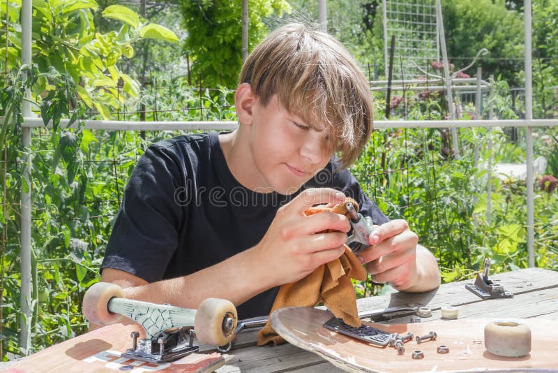 Il giovane tipo ripara le ruote su un pattino su una stalla di legno nel giardino fotografie stock Il giovane tipo ripara le ruote su un pattino su una stalla di legno nel giardino fotografie stock