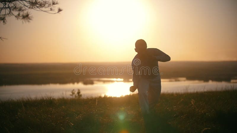 Il giovane uomo acrobatico esegue i trucchi marziali sulla collina al tramonto