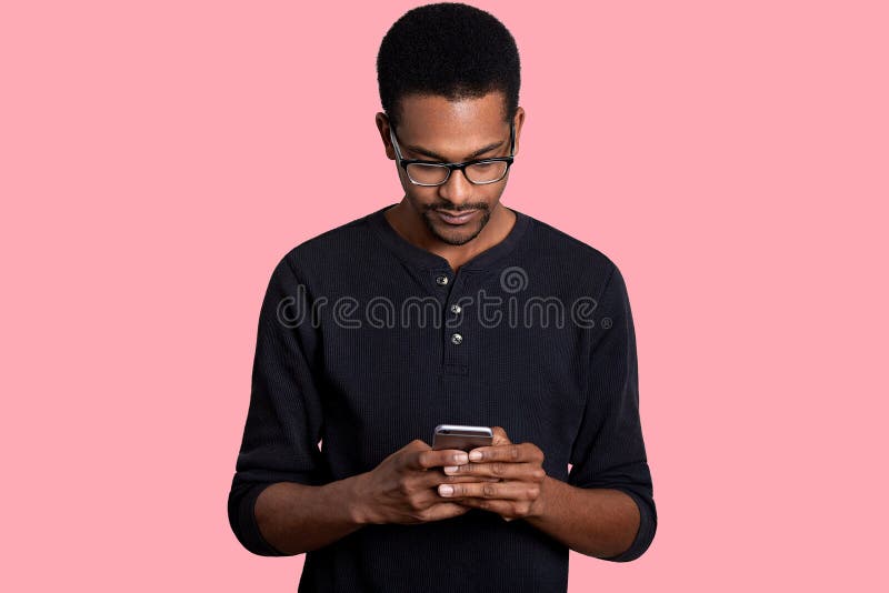 Il giovane uomo africano bello tiene lo Smart Phone, scarica gli archivi L'uomo pelato scuro veste l'attrezzatura casuale nera, u fotografie stock libere da diritti Il giovane uomo africano bello tiene lo Smart Phone, scarica gli archivi L'uomo pelato scuro veste l'attrezzatura casuale nera, u fotografie stock libere da diritti
