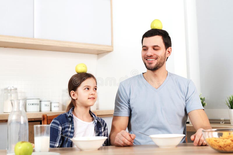 Il giovani papà e figlia divertenti si siedono accanto a ogni altro, mangiano i fiocchi di granturco deliziosi, tengono le mele s immagine stock Il giovani papà e figlia divertenti si siedono accanto a ogni altro, mangiano i fiocchi di granturco deliziosi, tengono le mele s immagine stock