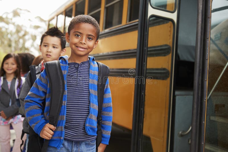 Il giovani scolaro ed amici neri aspettano per salire lo scuolabus immagini stock Il giovani scolaro ed amici neri aspettano per salire lo scuolabus immagini stock