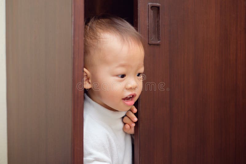 Il grazioso bambino di 18 mesi / 1 anno, piccolo bambino asiatico, con un maglione bianco, si nasconde nell'armadio a casa.