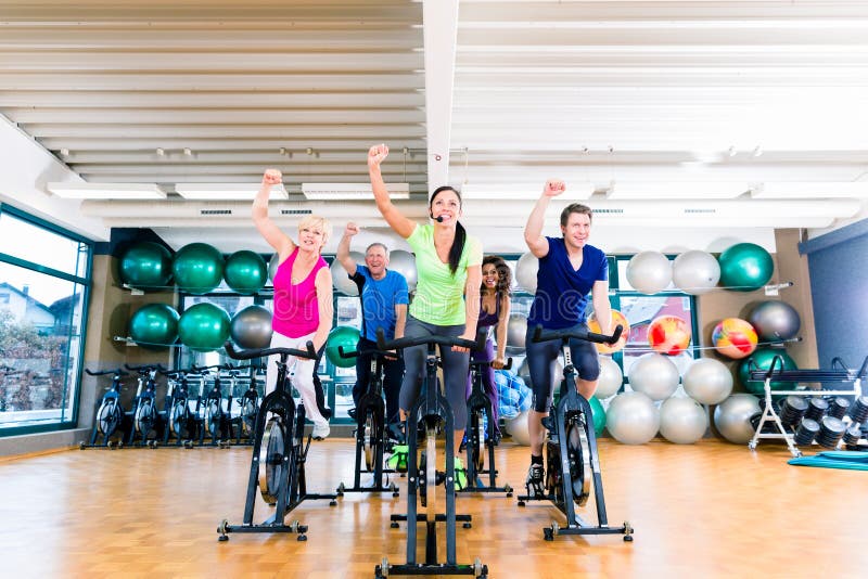 Il gruppo di uomini e di donne che filano sulla forma fisica bikes in palestra immagine stock Il gruppo di uomini e di donne che filano sulla forma fisica bikes in palestra immagine stock