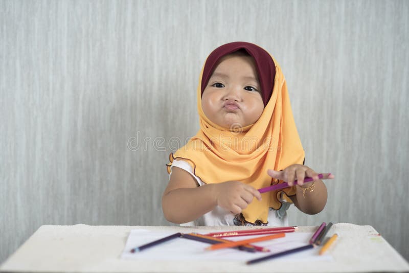 Il hijab d'uso asiatico neonata/del bambino sta divertendosi l'apprendimento utilizzare le matite mentre faceva il fronte diverte fotografia stock Il hijab d'uso asiatico neonata/del bambino sta divertendosi l'apprendimento utilizzare le matite mentre faceva il fronte diverte fotografia stock