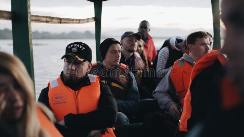 IL KENYA, KISUMU - 20 MAGGIO 2017: Gruppo di gente caucasica e di marinaio africano che si siedono in barca I turisti esplorano l fotografia stock IL KENYA, KISUMU - 20 MAGGIO 2017: Gruppo di gente caucasica e di marinaio africano che si siedono in barca I turisti esplorano l fotografia stock