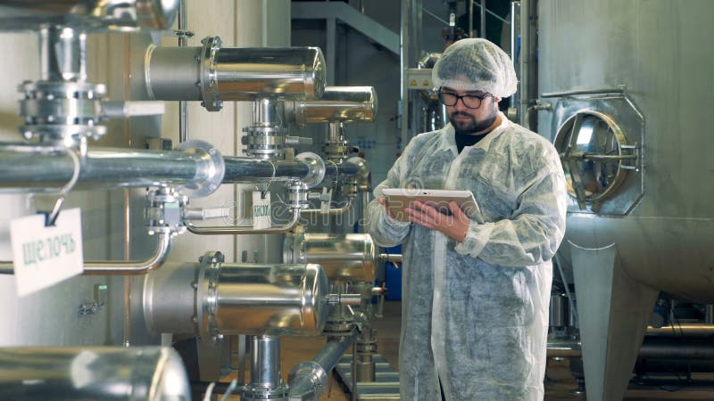 Il lavoratore della distilleria sta controllando un'unità con i tubi ed i bacini idrici