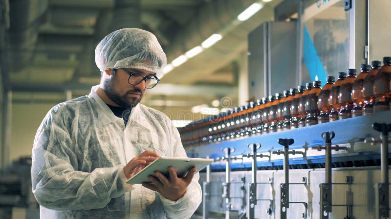 Il lavoratore della fabbrica di birra sta facendo funzionare una compressa mentre le bottiglie di birra riempite stanno muovendo