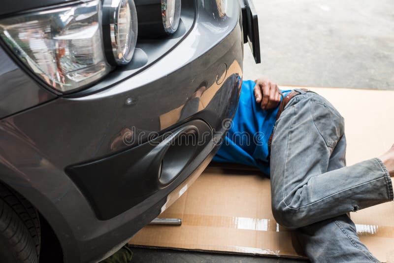Il lavoratore è sotto l'automobile per cambiare l'olio per motori immagini stock libere da diritti Il lavoratore è sotto l'automobile per cambiare l'olio per motori immagini stock libere da diritti