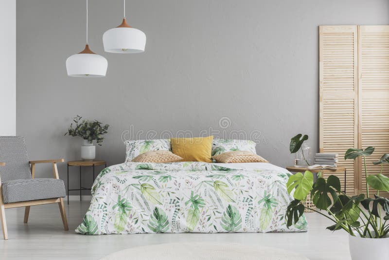 Il letto matrimoniale con gli accenti botanici sugli strati e sulla pesca ha colorato i cuscini in camera da letto scandinava gri fotografia stock Il letto matrimoniale con gli accenti botanici sugli strati e sulla pesca ha colorato i cuscini in camera da letto scandinava gri fotografia stock
