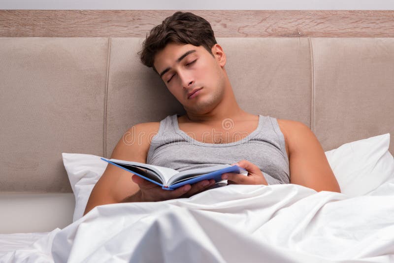 Il libro di lettura dell'uomo nel letto immagini stock Il libro di lettura dell'uomo nel letto immagini stock