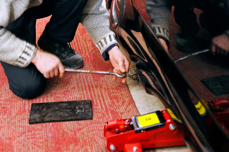 Il meccanico installa un martinetto idraulico meccanico e per la riparazione dell'automobile fotografie stock Il meccanico installa un martinetto idraulico meccanico e per la riparazione dell'automobile fotografie stock