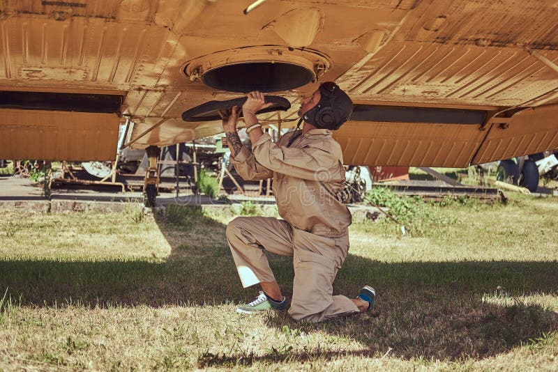 Il meccanico nel casco di volo e dell'uniforme ripara il vecchio aeroplano militare in un museo all'aperto fotografia stock libera da diritti Il meccanico nel casco di volo e dell'uniforme ripara il vecchio aeroplano militare in un museo all'aperto fotografia stock libera da diritti