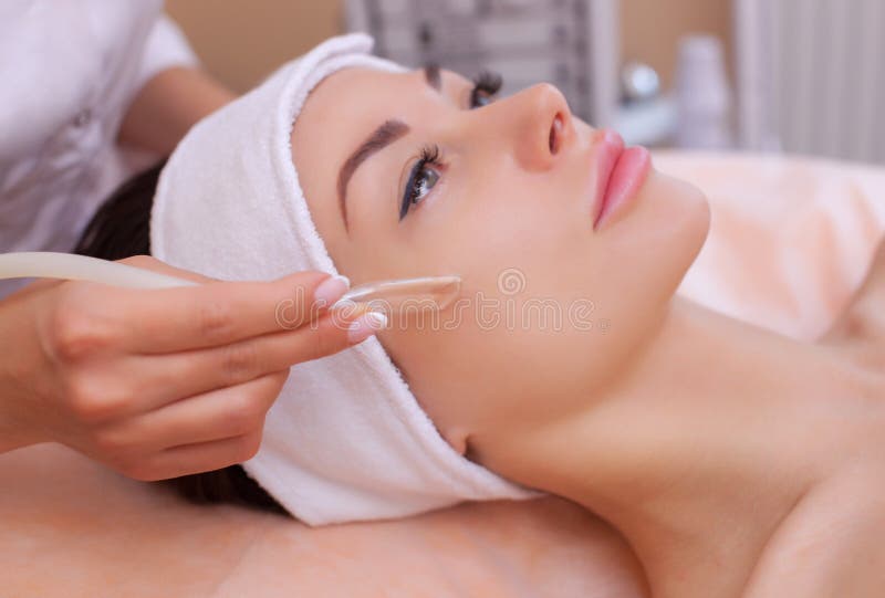 The doctor-cosmetologist makes the face vacuum therapy on the cheek of a beautiful, young woman in a beauty salon.Cosmetology and professional skin care. The doctor-cosmetologist makes the face vacuum therapy on the cheek of a beautiful, young woman in a beauty salon.Cosmetology and professional skin care.